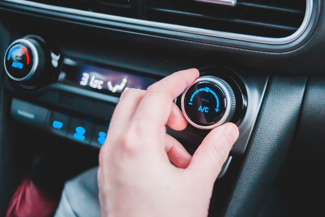 Een hand draait aan de airco-knop in een wagen