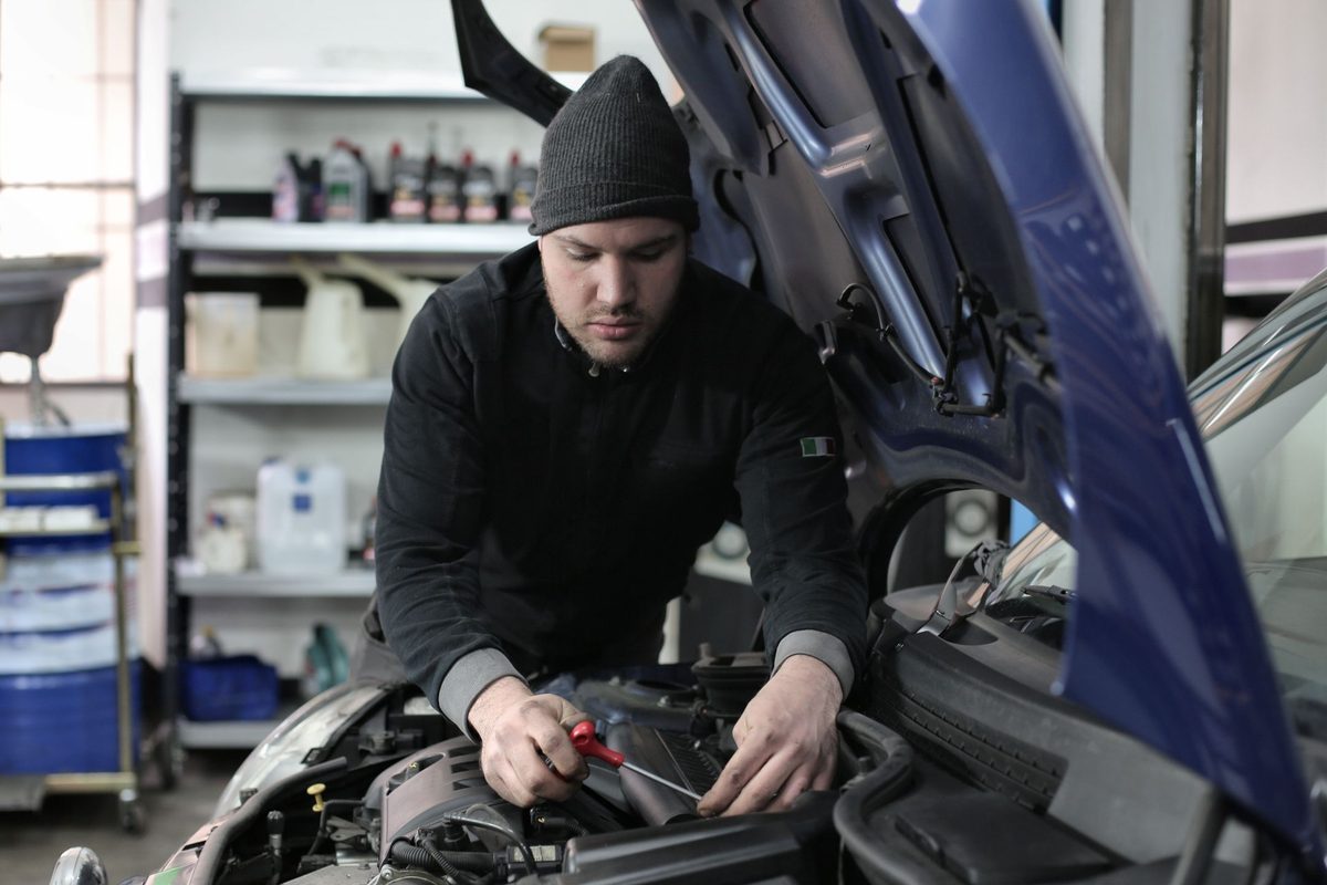Een mechanieker werkt met een schroevendraaier onder de open motorkap